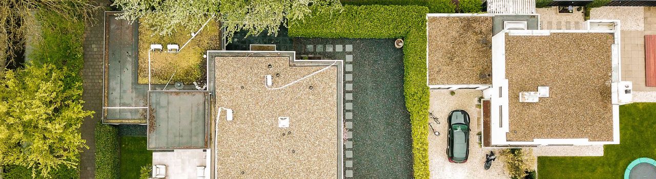 View of house and yard from above, showing roof, sidewalks, paved areas, and grassy areas.