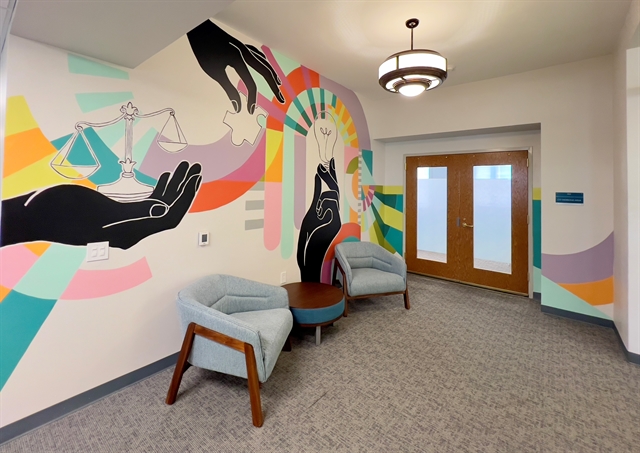 photograph of a mural with three hands working together, there is a pastel swirl of colors surrounding the hands that hold an old scale, puzzle piece and light bulb