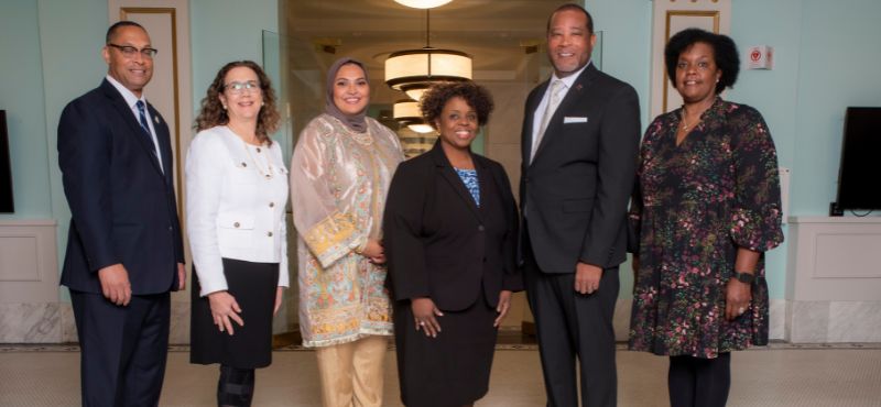 The Board of County Commissioners and County Manager pose for a photo in a hallway.