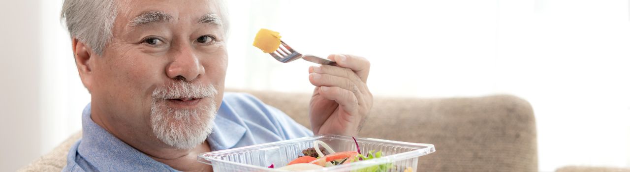 Older male holding up food on a fork.